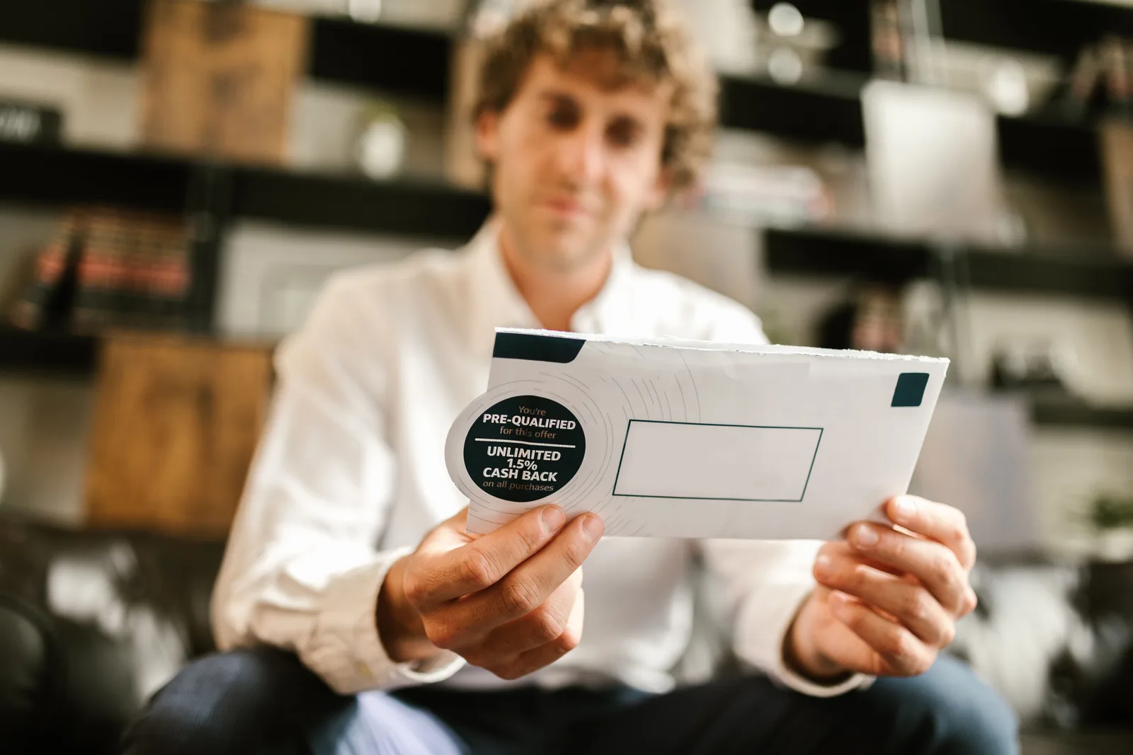 A man sitting indoors, reading an envelope with a cash back offer, blurred background. Common email design mistakes that quietly tank click-through rates