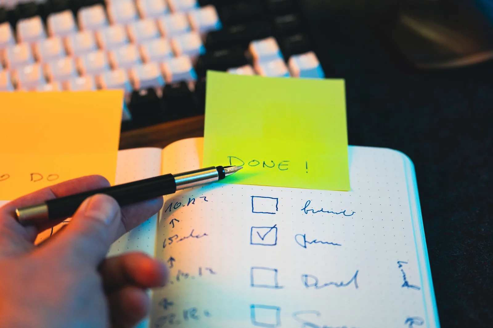 Close-up of hand holding pen over notebook checklist with sticky notes labeled 'DONE!'. A email marketing analytics checklist built for real conditions