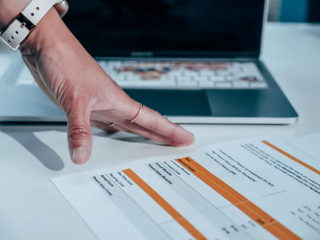 Close-up of a hand reviewing a financial report on a laptop, indicating focus on business analysis. Email marketing software pricing: buyer-side total cost