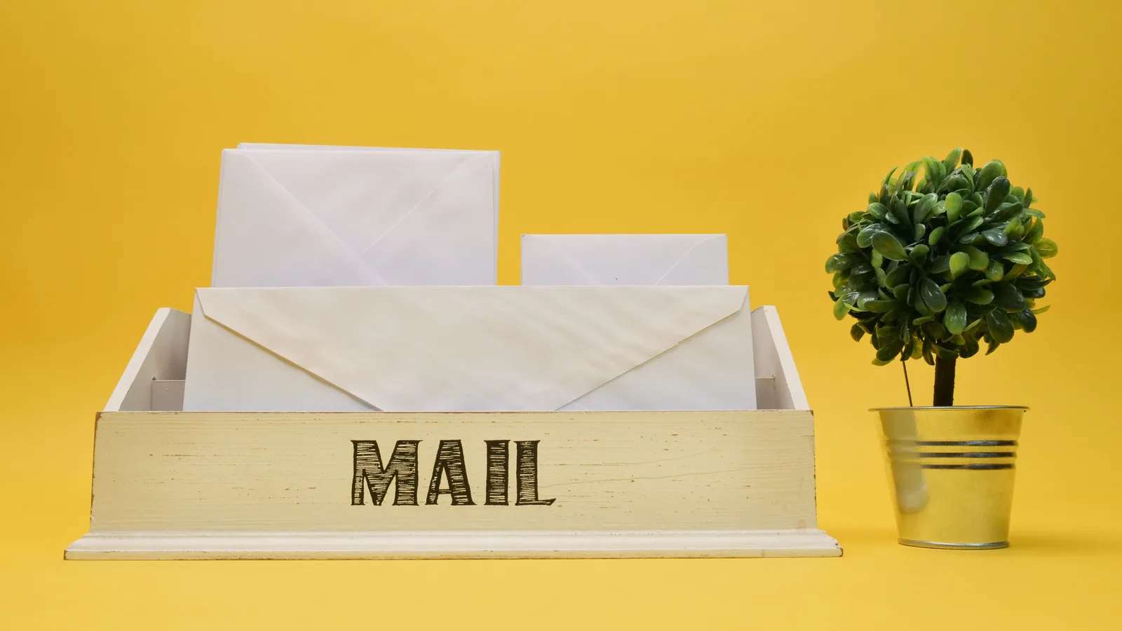 A wooden mail organizer with white envelopes and small potted plant on a yellow background. 9 things that decide email marketing strategy trends
